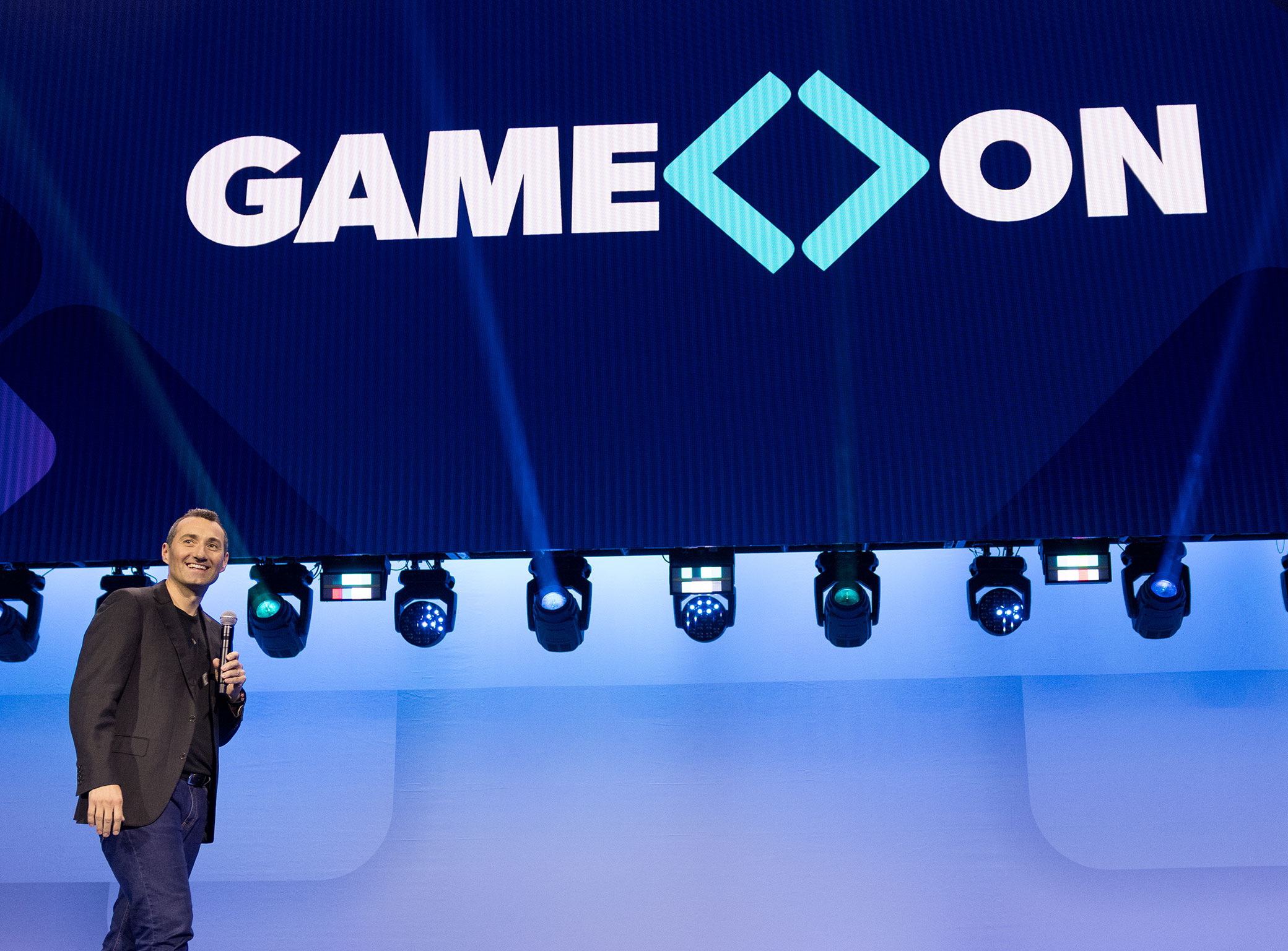 Chris smiles at associates in the audience at the Sam’s Club meeting with the words “Game On” appearing on the screen above.