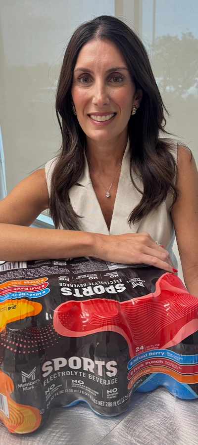 Sam's Club associate Bruna Fernandes sits at a table with her arm draped across a package of sports drinks.