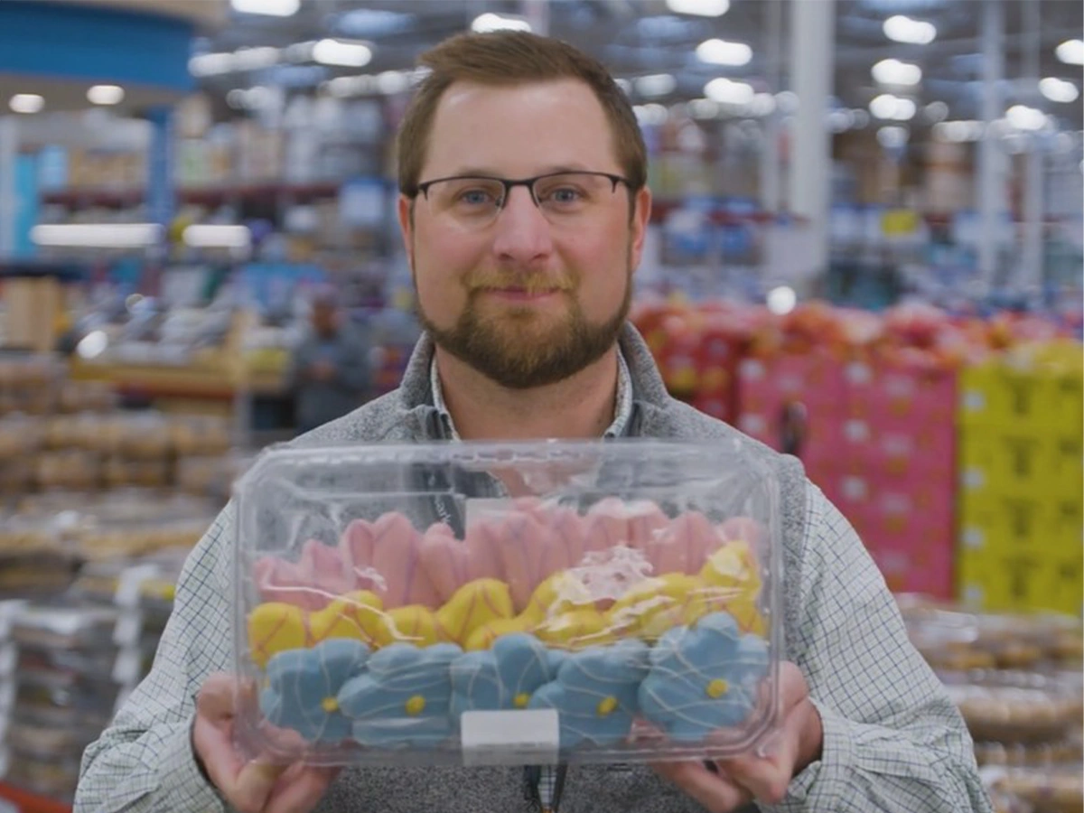 Sam's Club associate Garret Dietz smiles at the camera while holding a tray of colorful cookies.