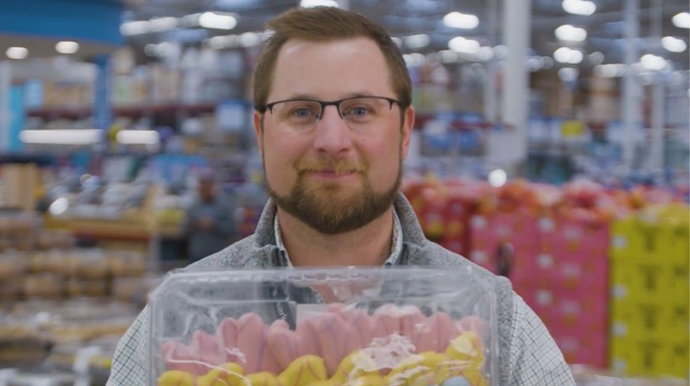 Sam's Club associate Garret Dietz smiles at the camera while holding a tray of colorful cookies.